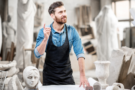 Portrait of a handsome male sculptor having an idea standing in the old atmospheric studio with sculptures on the backgroundの写真素材