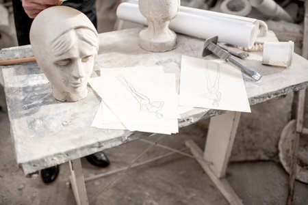 Working place with old sculptures, working tools and drawings on the table in the sculptors studio