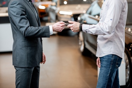 Salesperson giving keychain to a male client at the showroom with modern cars on the background, Close-up with no faceの写真素材