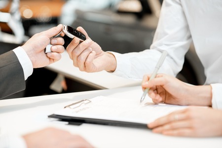 Salesperson giving a keychain from a new car to a client at the stand in the car showroom, close-up view with no faceの写真素材