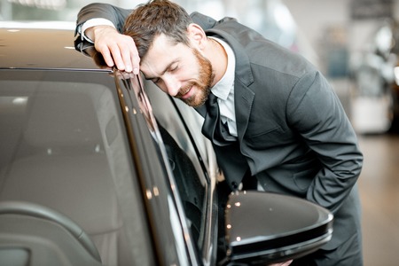 Businessman touching with face a new luxury car in the showroomの写真素材