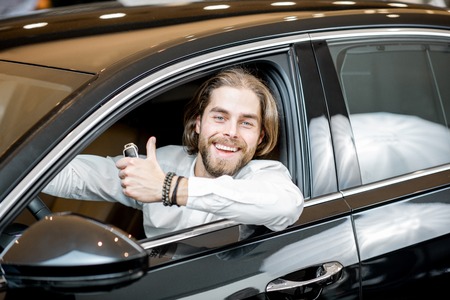 Portrait of a happy owner sitting on a driver seat of a new luxury car at the showroomの写真素材