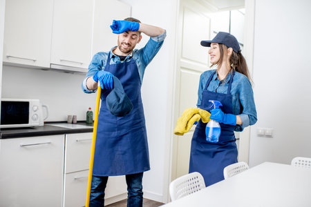 Portrait of a tired couple standing as a professional cleaners in uniform during the break in the...