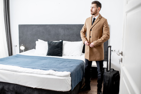 Businessman wearing coat standing with a suitcase at the hotel room before the check outの写真素材