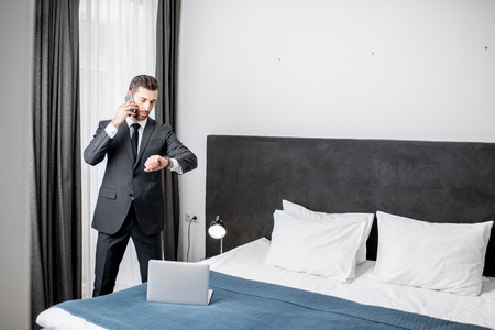 Elegant businessman talking phone near the window in the comfortable hotel room or bedroomの写真素材