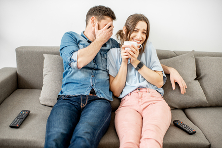 Young couple with scared emotions watching TV sitting together on the couch at homeの写真素材