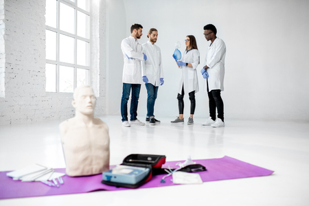 Group of young medics standing and talking together during the break of the first aid training with medical stuff and dummies on the floorの写真素材