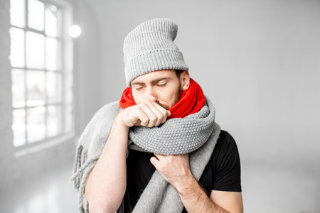 Portrait of a man wrapped in a warm scarves and hat feeling bad having a winter disease indoorsの写真素材