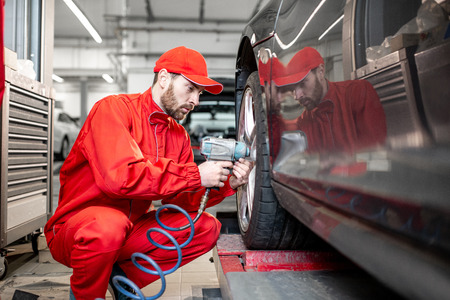 ar service worker in red uniform changing wheel of a sport car at the tire mounting serviceの写真素材