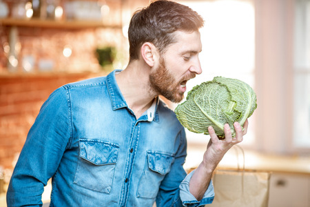 Portrait of a handsome man holding cabbage head on the kitchen. Healthy vegan food conceptの写真素材