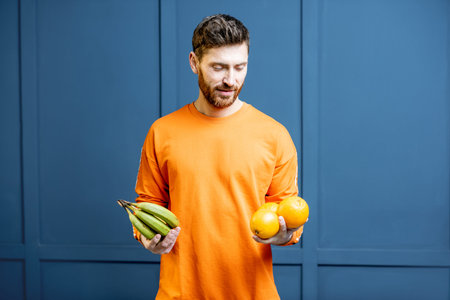 Colorful portrait of a caucasian bearded man in orange sweater holding fruits on the blue background