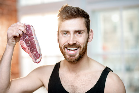 Portrait of a handsome sports man in black t-shirt with raw meat steak indoorsの写真素材