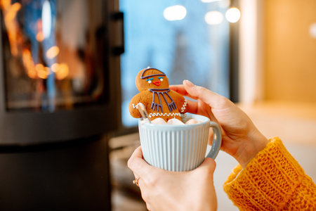 Woman holding Christmas gingerbread with cup near the fireplace at home
