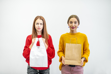 Portrait of a two women holding plastic and paper bags standing on the white background. Ecological in contrast to non recyclable packaging concept