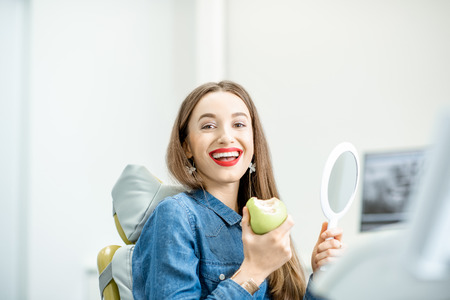 Portrait of a young beautiful woman with healthy smile sitting with green apple in the dental officeの写真素材