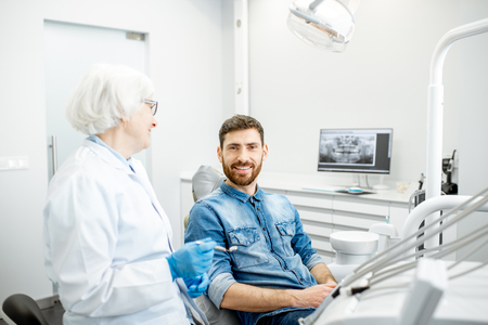 Portrait of a handsome male patient in blue shirt with elderly woman dentist in the dental officeの写真素材