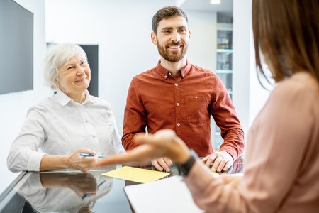 Smiling man with his senior mother talking with receptionist in the hospitalの写真素材