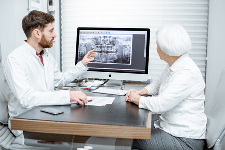 Senior woman patient during the medical consultation with dentist showing dental x-ray on the...