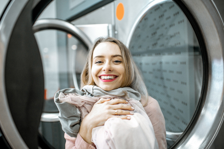 Portrait of a cheerful woman with clean and dried clothes in the laundryの写真素材