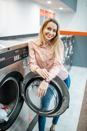 Portrait of a young smiling woman standing in the self-service public laundryの写真素材