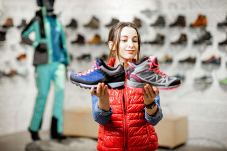 Young woman choosing trail shoes for mountain hiking in the modern sports shopの写真素材