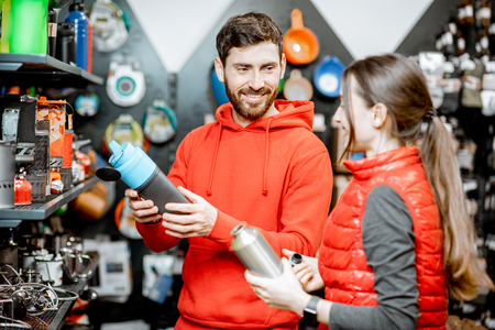 Young couple dressed in red sportswear choosing dishes for camping in the shop with travel equipmentの写真素材