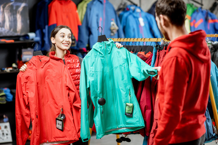 Young woman choosing between red and turquoise jacket standing with boyfriend in the sports shopの写真素材