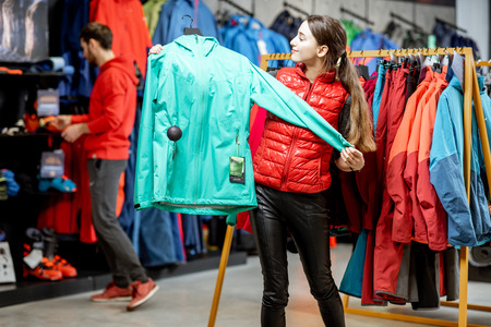 Young woman choosing winter clothes trying windbreaking jacket in the sports shopの写真素材