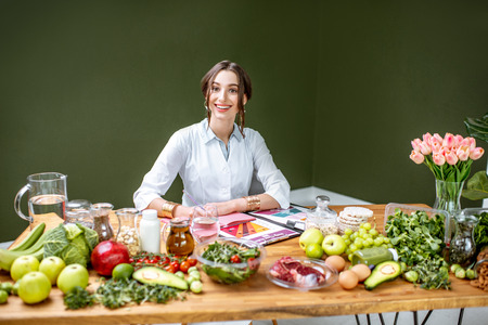 Woman dietitian in medical uniform working on a diet plan sitting with different healthy food ingredients in the green officeの写真素材