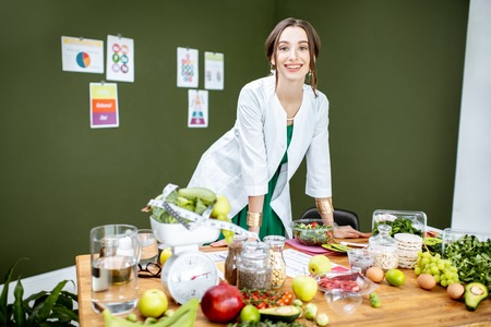 Portrait of a young woman nutritionist standing near the table full of healthy products in the green officeの写真素材