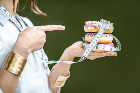 Woman showing on the sweet donuts on the green background. Unhealthy eating and adiposity conceptの写真素材