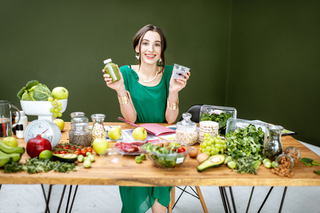 Portrait of a beautiful woman as a dietitian sitting with smoothie, chia pudding and various healthy food ingredients in the green officeの写真素材