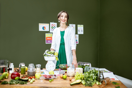 Portrait of a young woman nutritionist standing near the table full of healthy products in the green officeの写真素材