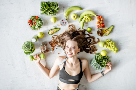 Beauty portrait of a sports woman surrounded by various healthy food lying on the floor. Healthy eating and sports lifestyle conceptの写真素材