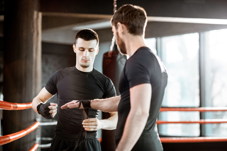 Boxing trainer winding bandage on the wrist for a man, preparing for the boxing on the boxing ring at the gymの写真素材