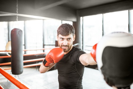 Athletic man fighting during the training with boxing trainer on the boxing ring at the gymの写真素材
