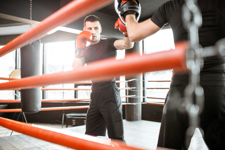 Athletic man fighting during the training with boxing trainer on the boxing ring at the gymの写真素材