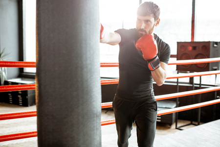 Athletic man in black sportswear training to box with punching bag on the boxing ring at the gymの写真素材