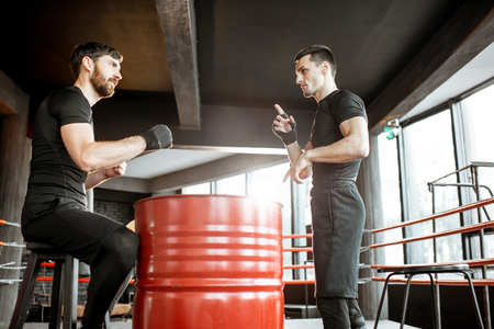 Boxing trainer showing to a man how to fight, teaching to box in the boxing ring at the gymの写真素材