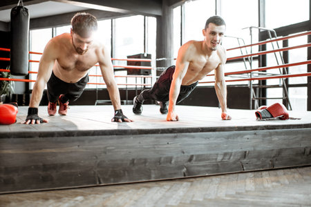 Two athletic men doing push-ups on the boxing ring, training before boxing at the gym