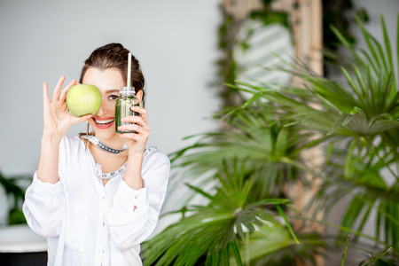 Portrait of a young woman with apple and smoothie drink indoors. Healthy eating and wight loss conceptの写真素材
