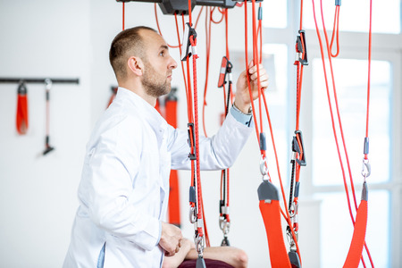 Senior physiotherapist doing treatment to a man with spine problems with suspension medical equipment at the rehabilitation clinicの写真素材