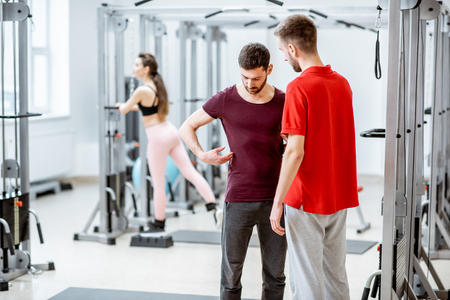 Therapist talking with man patient having problems with his back standing at the rehabilitation gymの写真素材