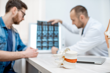Man during the medical consultation with senior therapist at the office. Image focused on the vertebral model on the foregroundの写真素材
