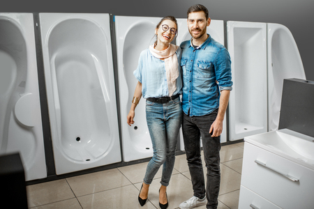Portrait of a young lovely couple choosing new bathroom furniture standing near the showcase with white acrylic bathtubs in the plumbing shopの写真素材