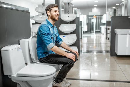 Man choosing lavatory pan sitting on it in the building shop with sanitary ceramicsの写真素材