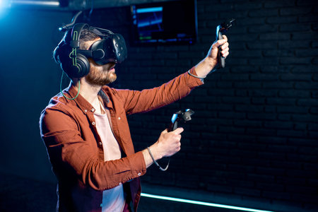 Man playing game using virtual reality headset and gamepads in the dark room of the playing club