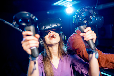 Man and woman playing game using virtual reality headset and gamepads in the dark room of the playing clubの写真素材