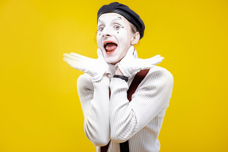 Portrait of an actor as a pantomime with white facial makeup showing expressive emotions on the yellow background indoorsの写真素材