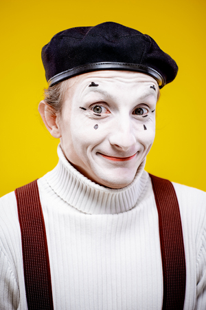 Close-up portrait of an actor as a pantomime with white facial makeup showing expressive emotions on the yellow background indoorsの写真素材